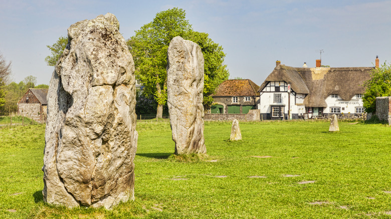 Ancient standing stones in grass field with thatched roof pub in Avebury, England