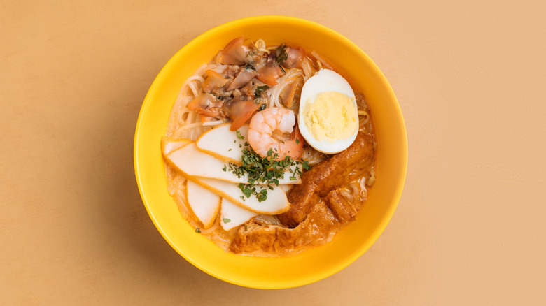 Laska soup with and egg, shrimp, noodles, and other ingredients in a yellow bowl