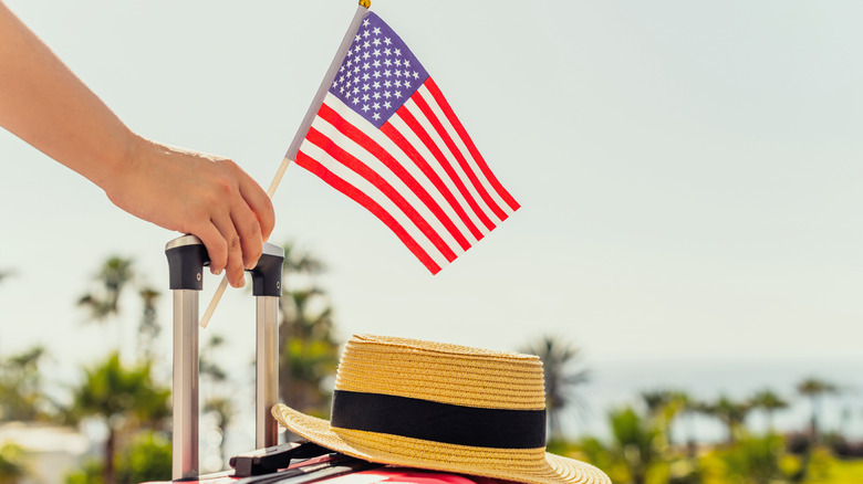 Traveler with case and hat holding American flag