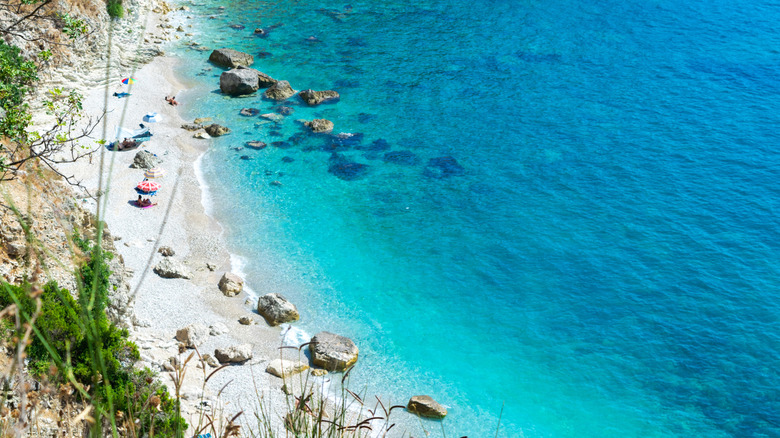 A high-angled view of a thin pebble beach in Himarë, half-submerged rocks, and turquoise water