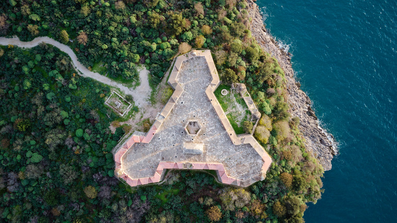 A drone shot of an old castle fortress in Himarë surrounded by vegetation and rocky cliffs by the sea