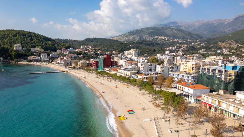 An aerial view of Himarë's sand bay backed by low buildings and stony hills in the distance