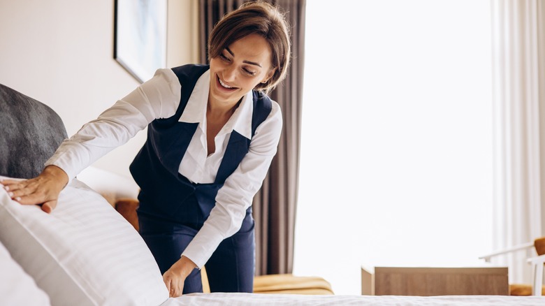 a housekeeper fluffs pillows in a hotel room