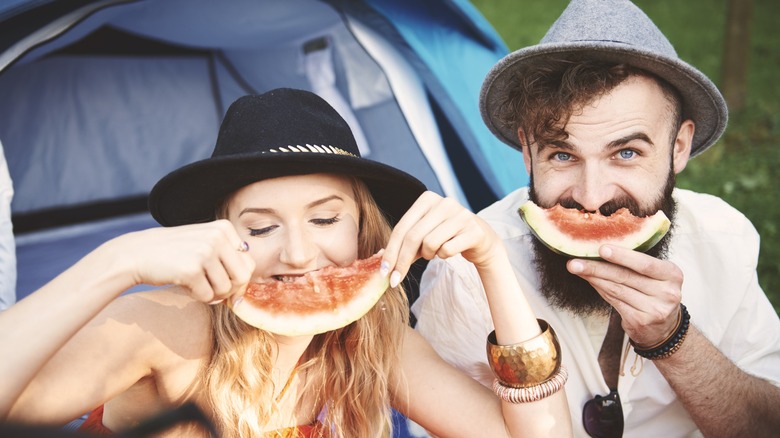 A woman and man wearing hats and eating watermelon