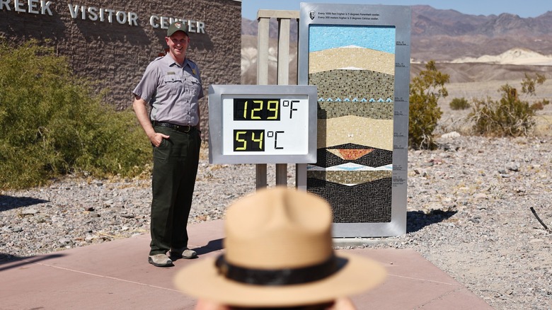 Park ranger in front of high temperature sign at Furnace Creek Visitor Center, Death Valley