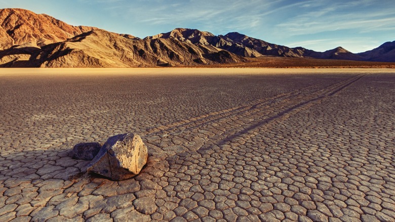 Large stone in cracked earth in front of mountains in Death Valley