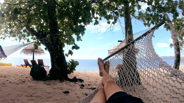 A first-person perspective lying in a net hammock on the beach at Likuri Island Resort