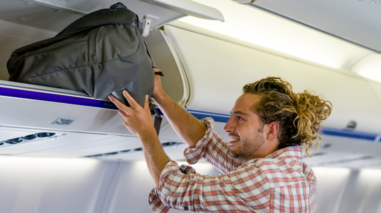 Smiling man putting bag in overhead compartment