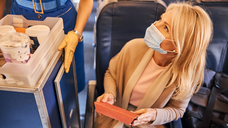 Passenger handing her trash to a flight attendant