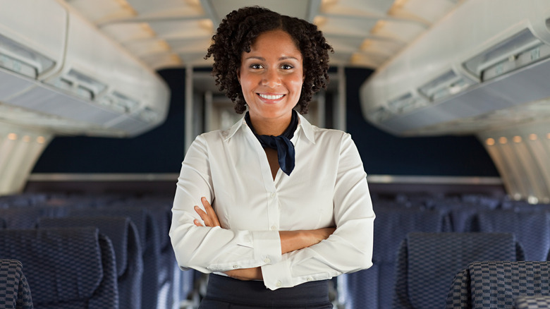 Flight attendant smiling with arms crossed in an empty plane