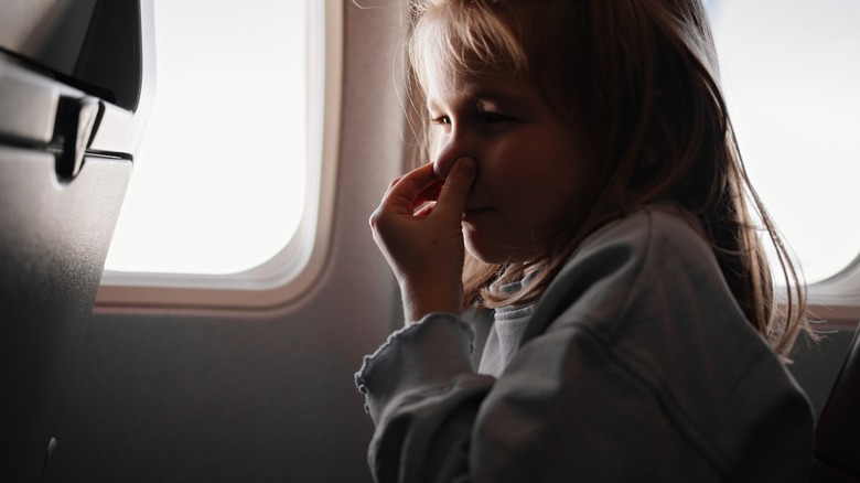 Child holding nose while on a plane