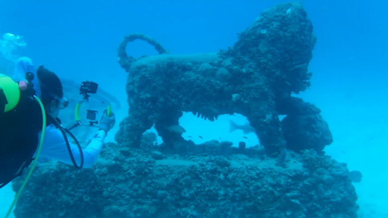 A diver photographs the statue of a lion underwater