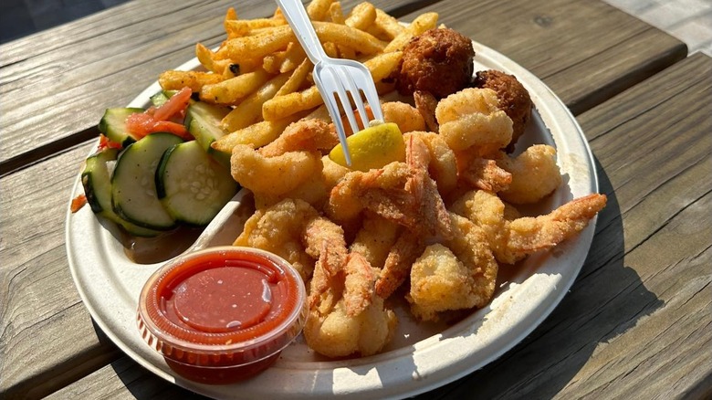 A plate of fried gulf shrimp, cucumber salad, and fries from Stewby's Seafood Shanty on a wooden table