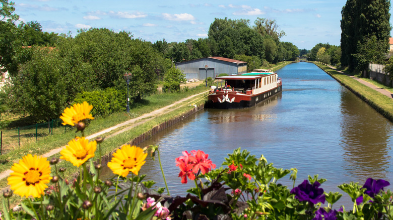 House barge on rural tree-lined canal with flowers in Alsace