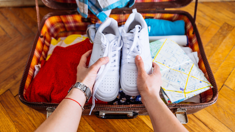 Person packing sneakers into a suitcase.