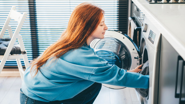 A young woman loading a washing machine.