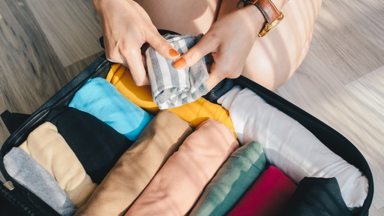 Woman packing rolled clothes into a suitcase.