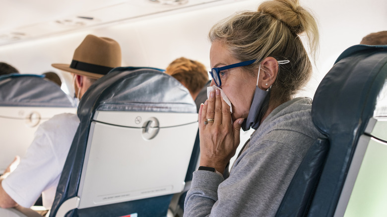 woman sick airplane blowing nose