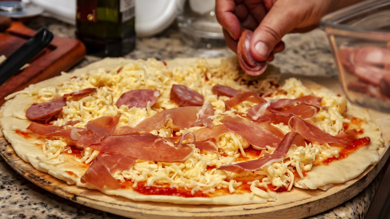 Person putting pepperoni slice on pizza