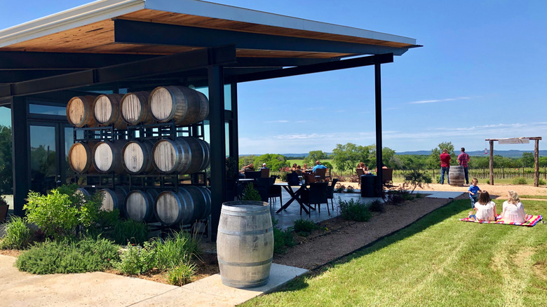 The outdoor patio of a Dripping Springs winery on a hill bordered by wine barrels on a sunny day