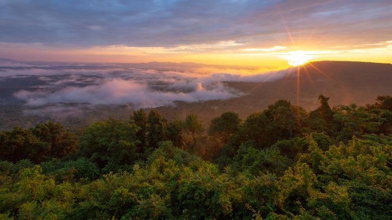 Sun peeking behing the mountains at the Arkansas Grand Canyon with cloud cover and green foliage