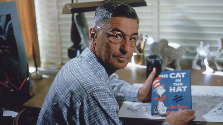 Dr. Seuss holding a copy of "The Cat in the Hat" at a table