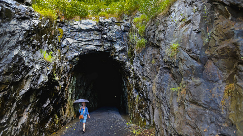 Women with umbrella walking out of rock tunnel