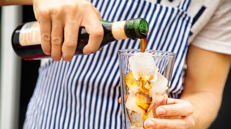 Server with striped apron pours fernet into iced glass