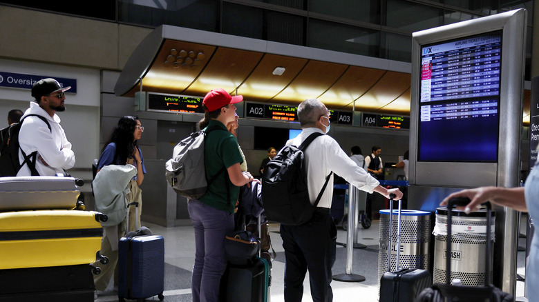 People with suitcases looking at an airport departure board