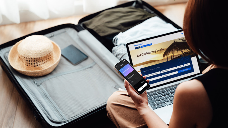 A woman researching flights with a packed suitcase in front of her