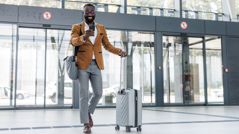 Man enters airport with roller suitcase.