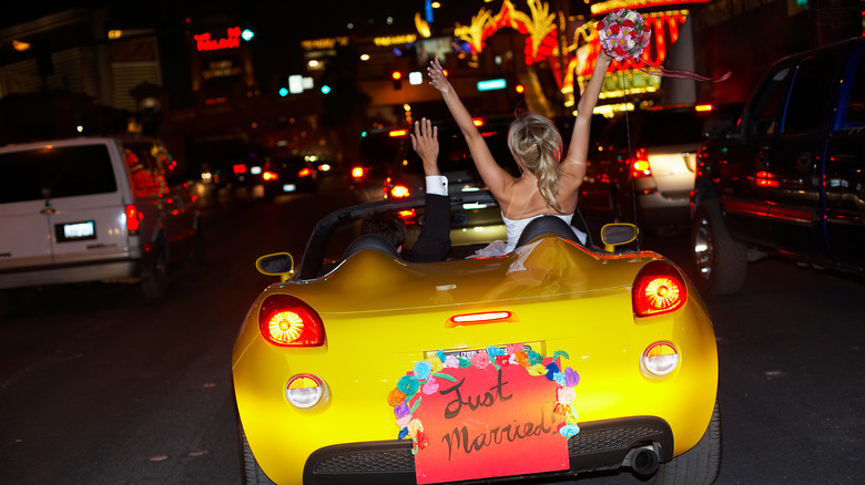 Bride and groom in Vegas, celebrating in a yellow sports car that says 