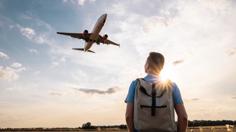 Man with backpack looking at airplane taking off