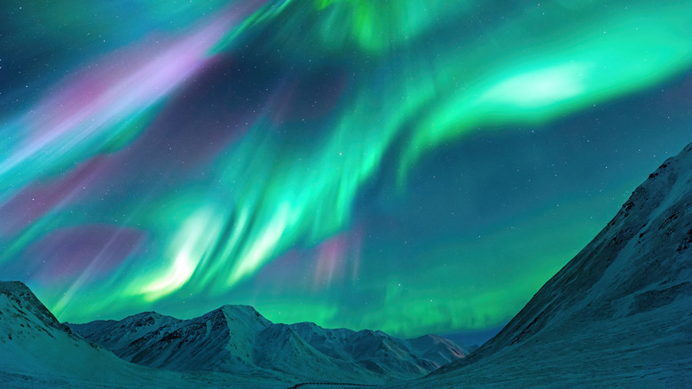 Pink and green northern lights over mountains