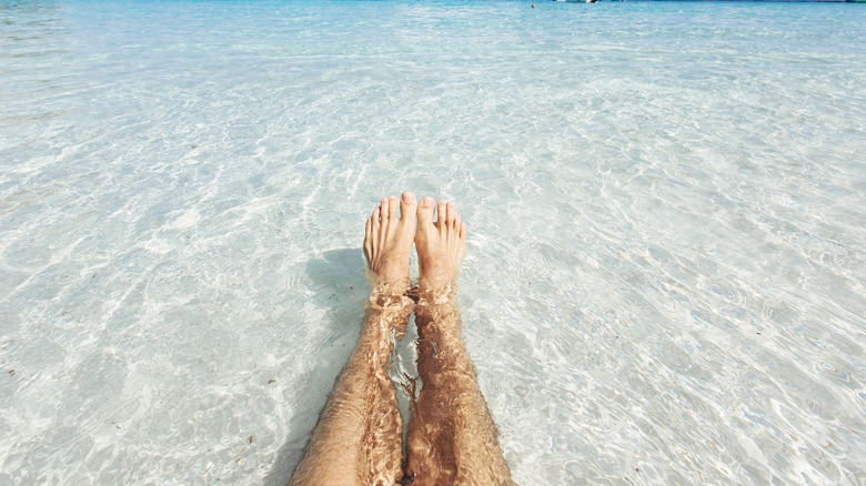 A person's bare legs in the ocean shallows.