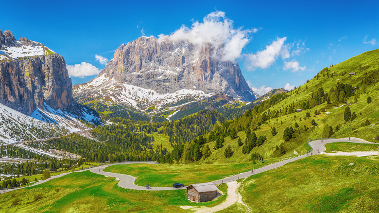 Green valley with windy roads and limestone mountain with scattered snow against a blue sky