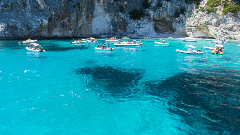 Boats anchored around the bright blue water of Pools of Venus, Sardinia