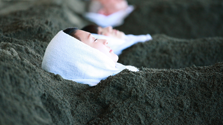 Several people lay in hot sand baths side by side