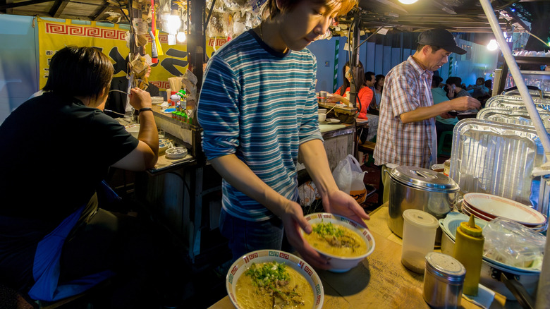 A shop vendor preparing ramen bowls in a yatai