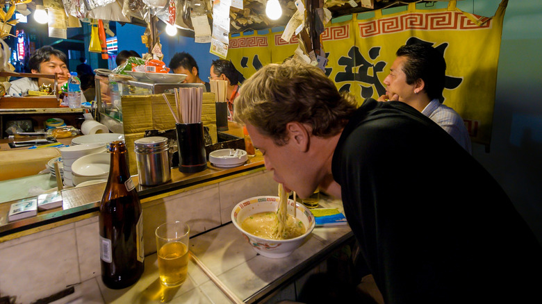 A tourist eating a bowl of noodles with a beer in a Fukuoka yatai