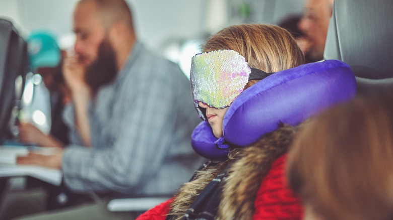 Girl sleeping on plane with neck pillow and eye mask