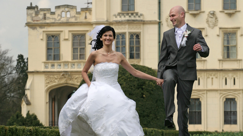 smiling bride and groom running in front of baroque building