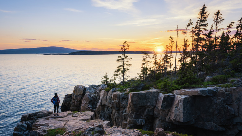 A hiker watches the sunset from the Schoodic Peninsula, Acadia National Park