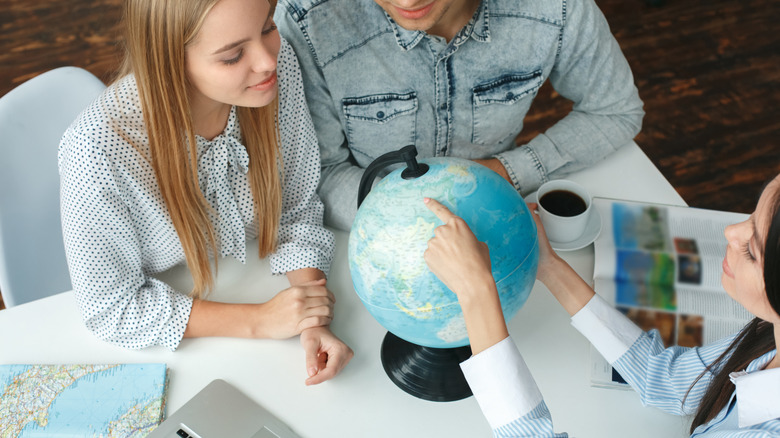 Couple sits with a travel agent pointing at a globe