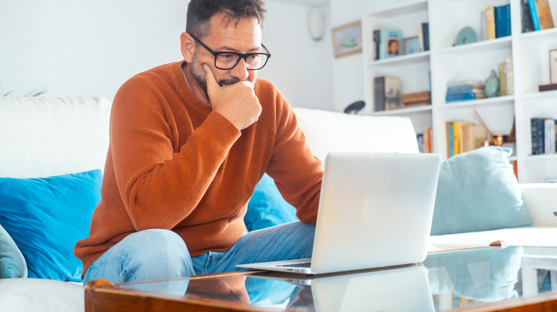 Man on sofa looks thoughtfully at laptop screen