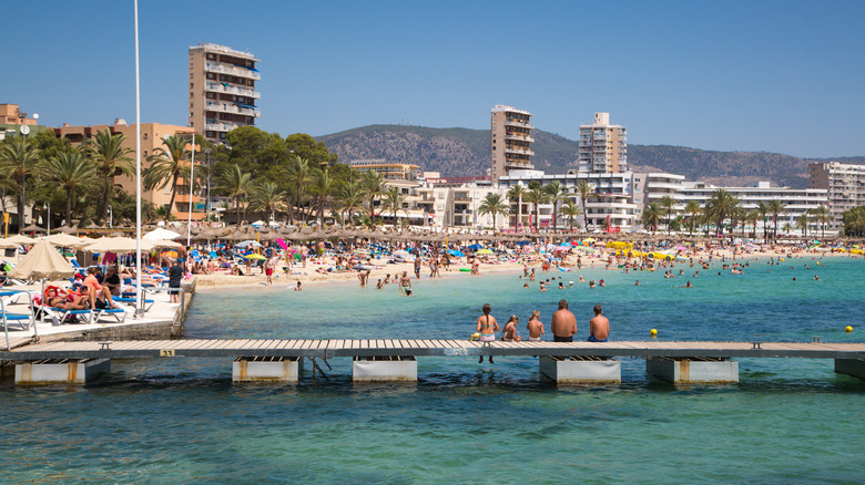 People sitting on a pier with crowds on the beach in the background in Magaluf, Mallorca, Spain