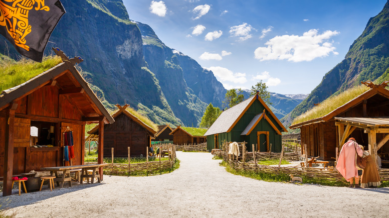 A traditional Viking village against a backdrop of mountains and blue skies.