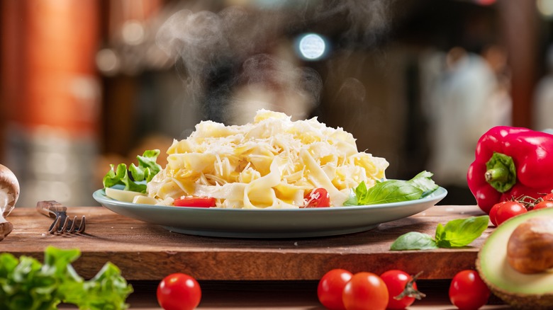 Steaming pasta dish featuring lettuce, bell peppers, and fresh tomatoes topped with parmesan