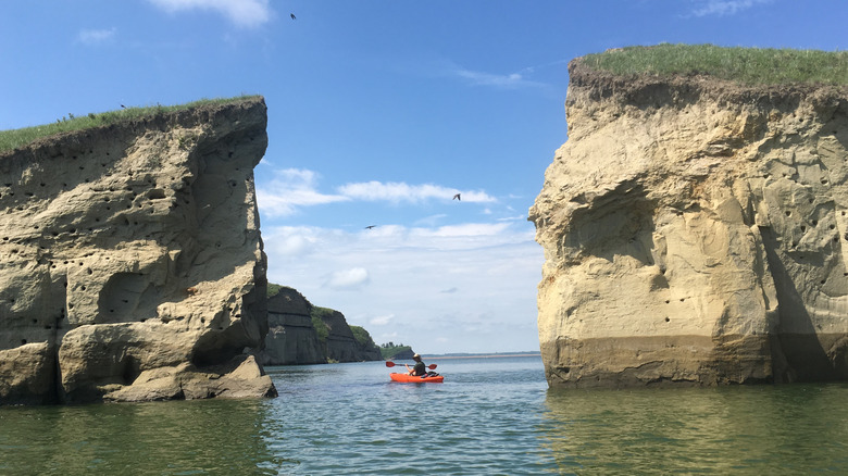 Person kayaking between rugged rock formation in Lake Sakakawea