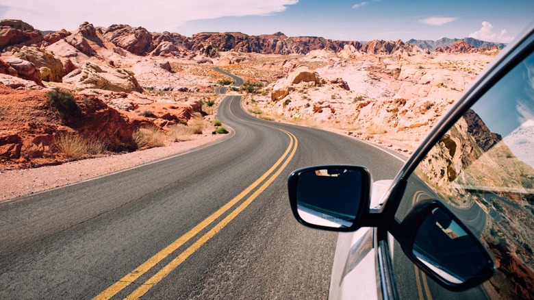 Car driving through a red-rocked desert terrain.